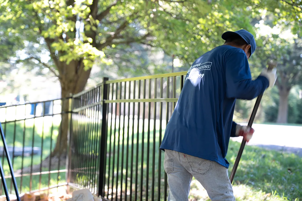 Crew member finishing grade along a new aluminum fence line, under Our Fencing Projects