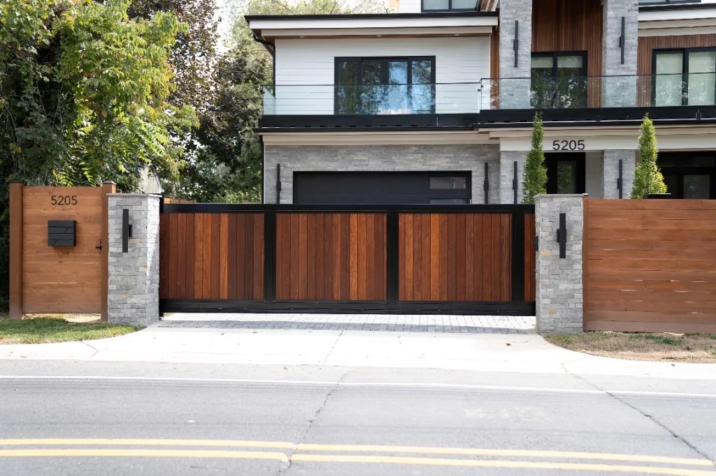 Modern wood sliding driveway gate with black metal frame and stone pillars at a Northern Virginia home, under Our Fencing Projects
