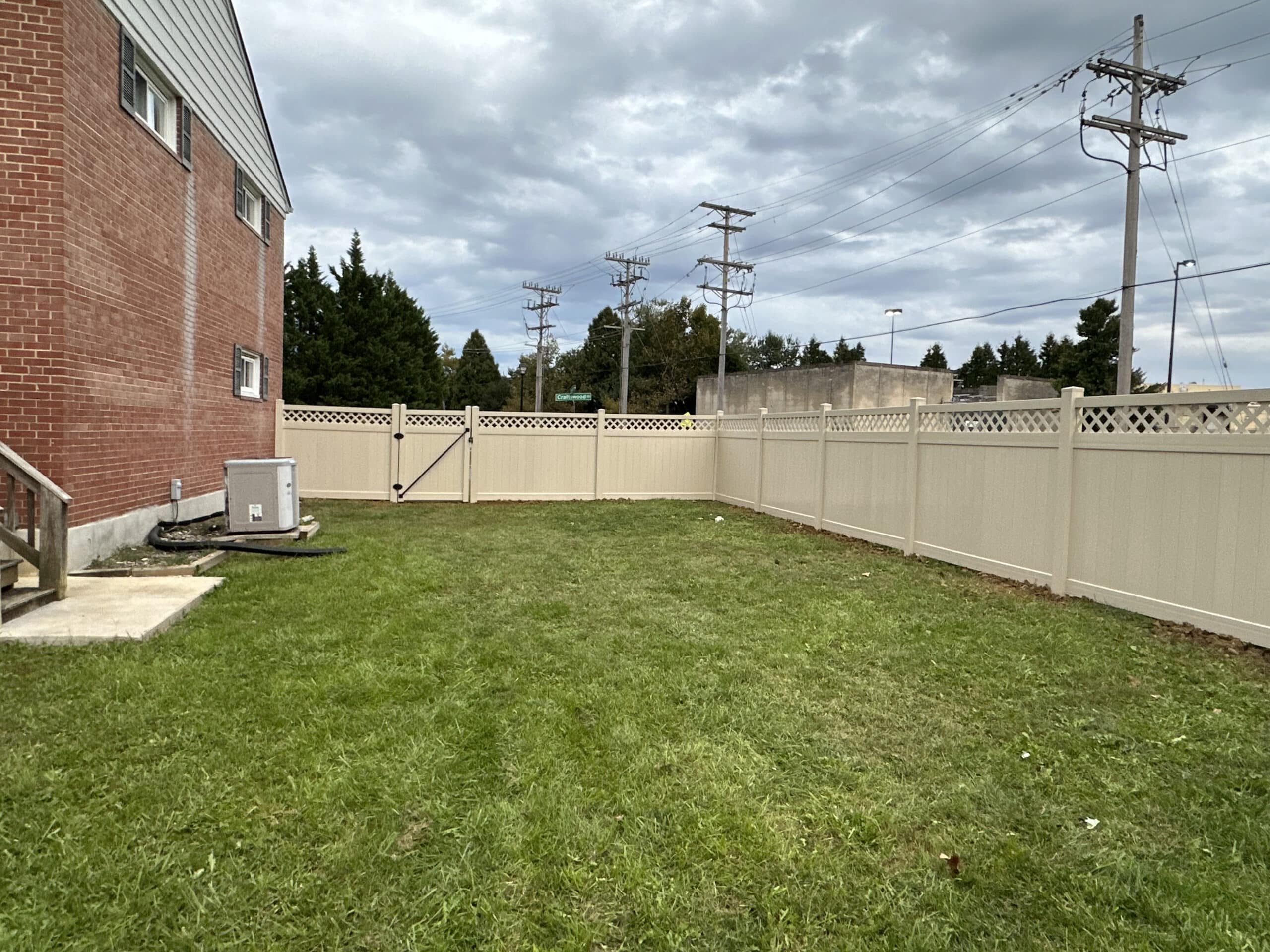 Privacy-focused tan vinyl fence lining a residential backyard with lush green grass and mature trees, in the late afternoon light, reflecting tranquility and neat landscaping.