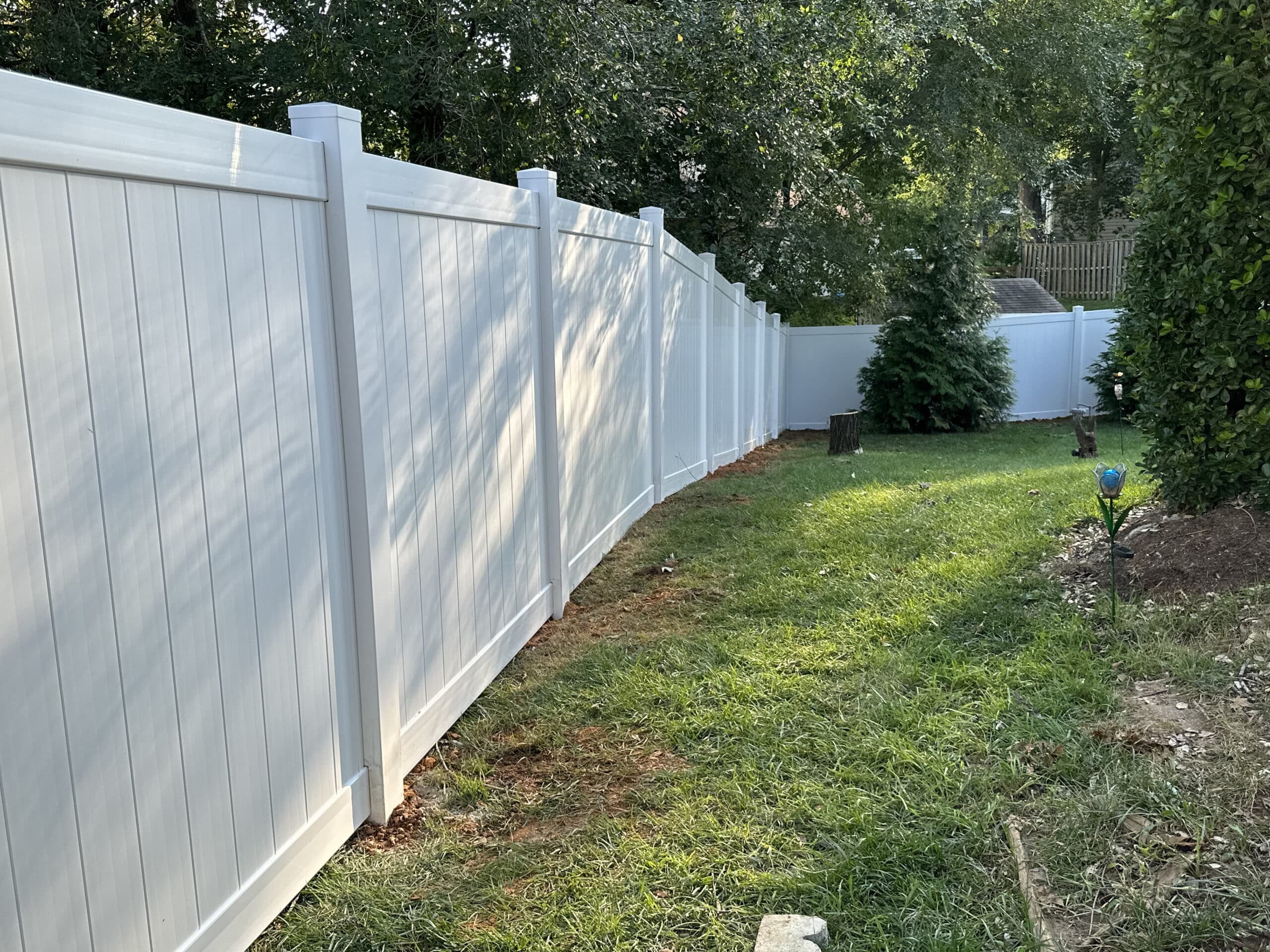 Privacy-focused white vinyl fence lining a residential backyard with lush green grass and mature trees, in the late afternoon light, reflecting tranquility and neat landscaping.